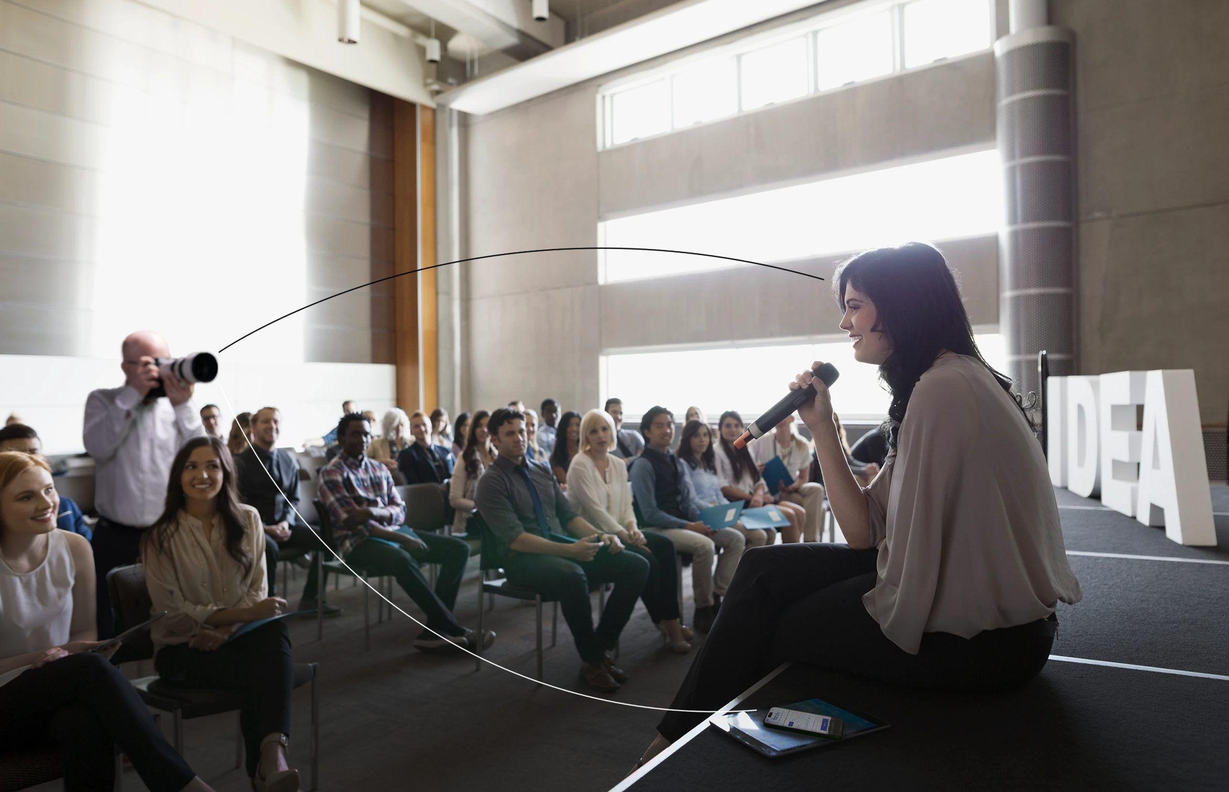 A photographer shoots a speaker on stage; the photo lands on an attendee’s phone